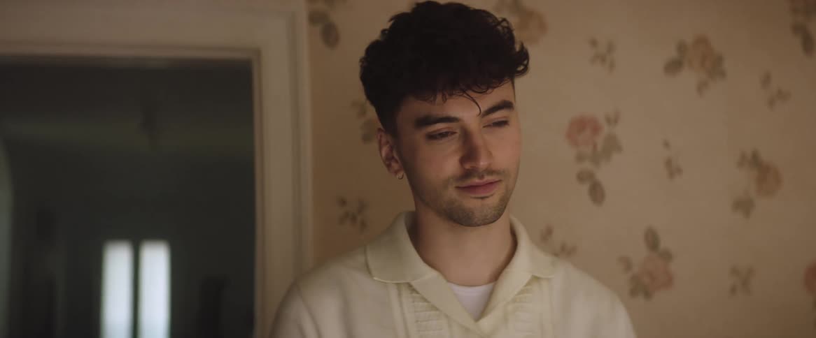 A man is standing in a room in deep thought as he cracks a smile