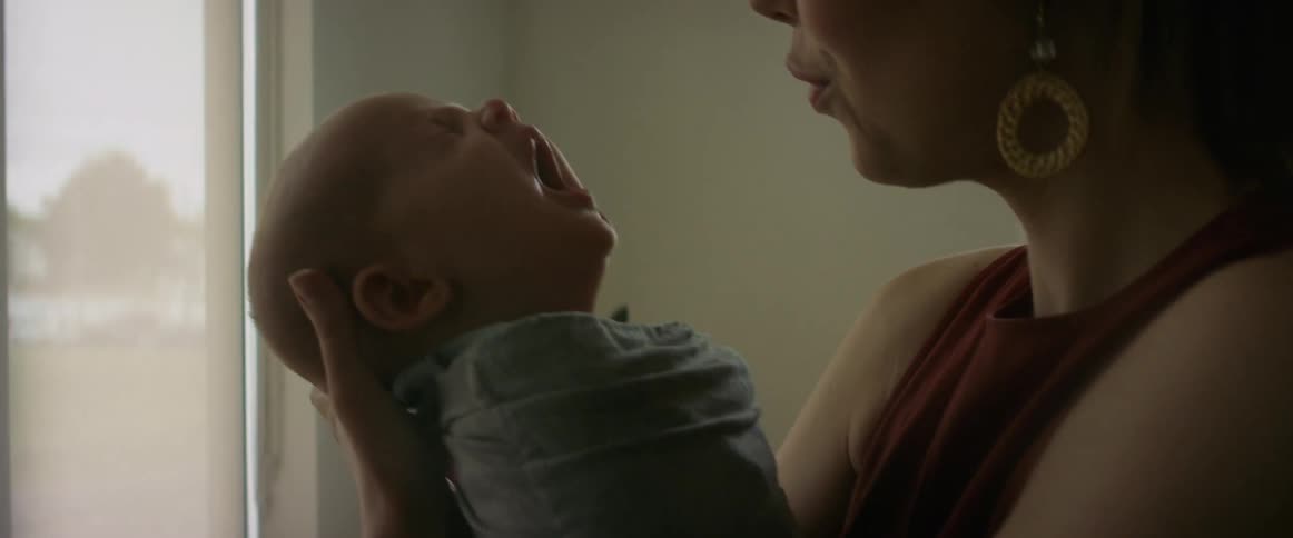 Mother with glasses earrings and blouse holds yawning baby