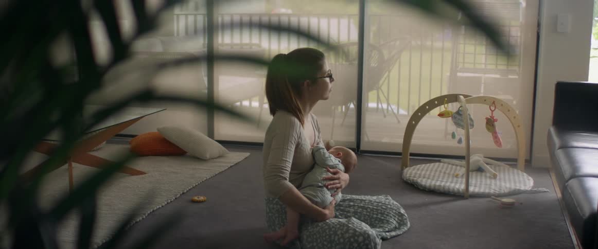 A mother nurses her baby in her arms sitting on the living room floor