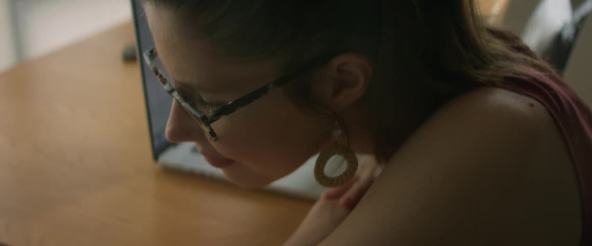 A woman sitting at a desk wearing glasses and earrings