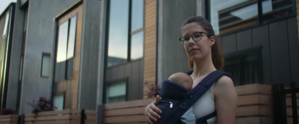 Mother stands near apartment buildings with baby in a carrier