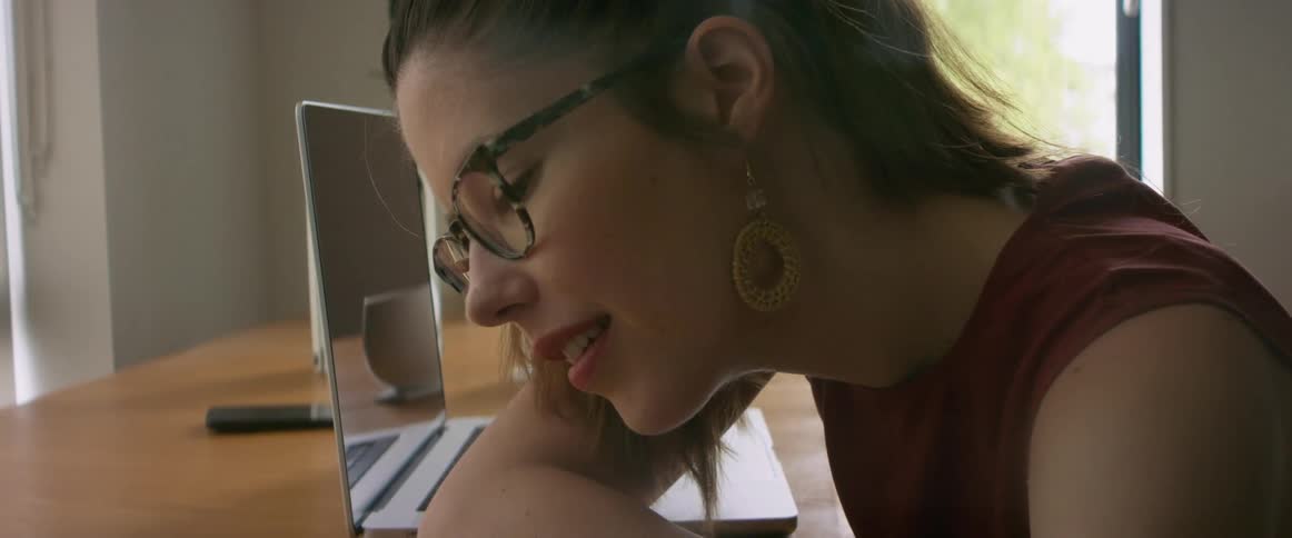 Woman with glasses sitting at desk in office talking on speakerphone