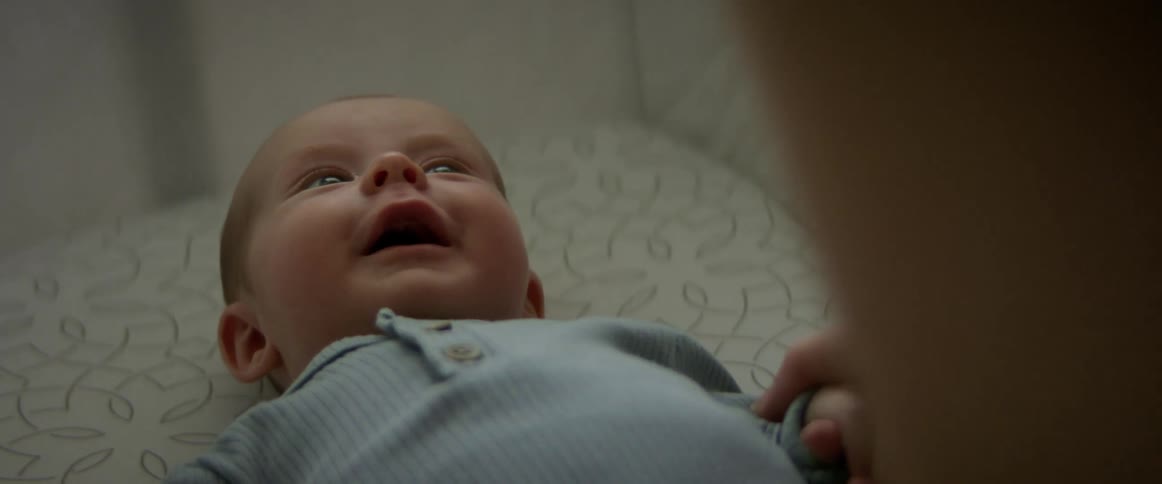Happy newborn baby laying in a baby crib looking up at an adult smiling