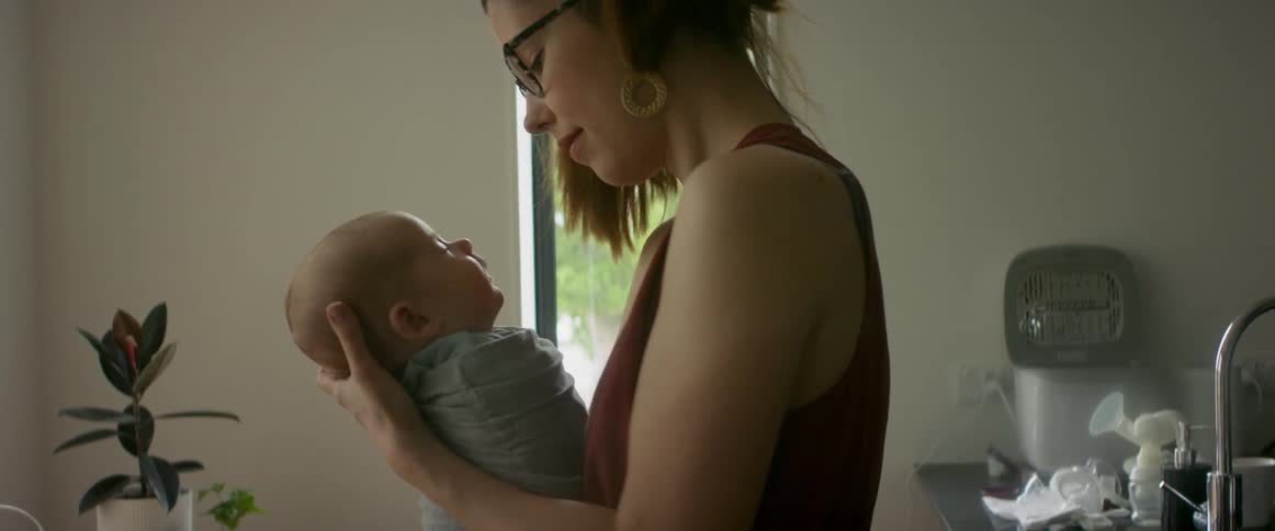 A woman stands at home and rocks her baby in her arms
