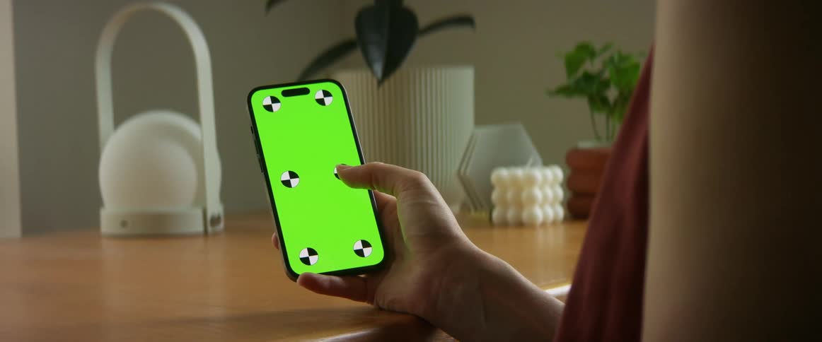 A person is holding a smartphone in their hand that is resting on a table and they are selecting one of six black and white circles on a green screen