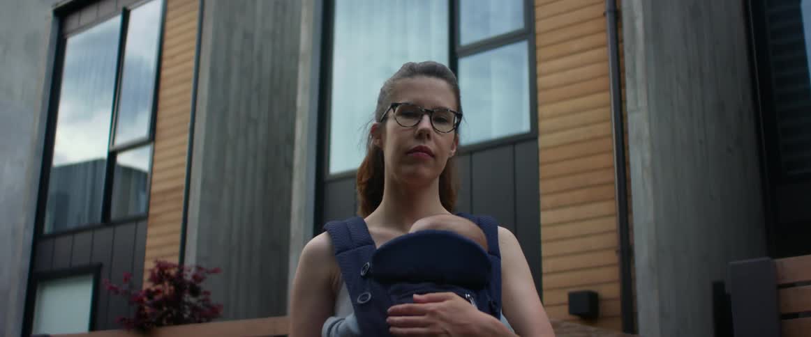 A mother holding her baby in a front carrier while she stands outside of a building