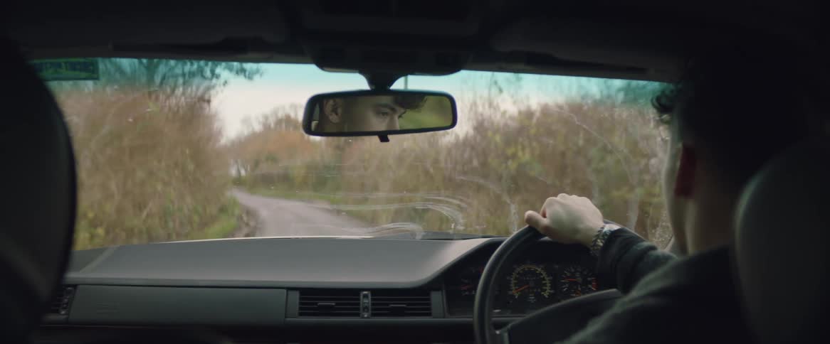 A man drives a car down a road with trees on both sides