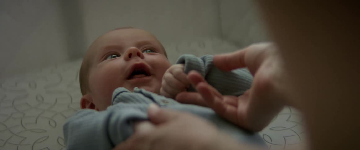 Mother ticking the nose of her newborn baby in the crib at home