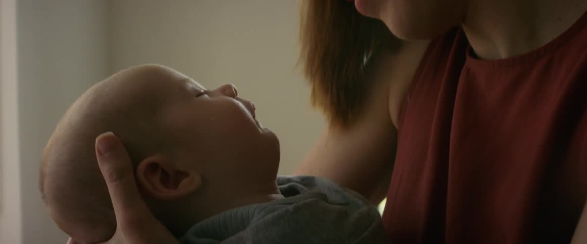 Blonde mother with red blouse holds baby son smiling at each other in the living room
