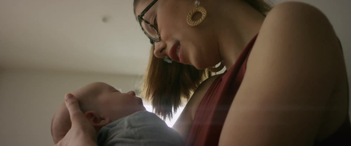Woman with glasses earrings and red blouse holds baby smilingly in the living room