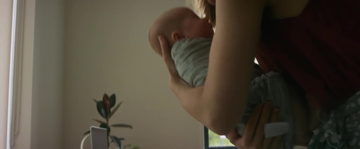 Woman with glasses earrings and red blouse picks up newborn baby son in room