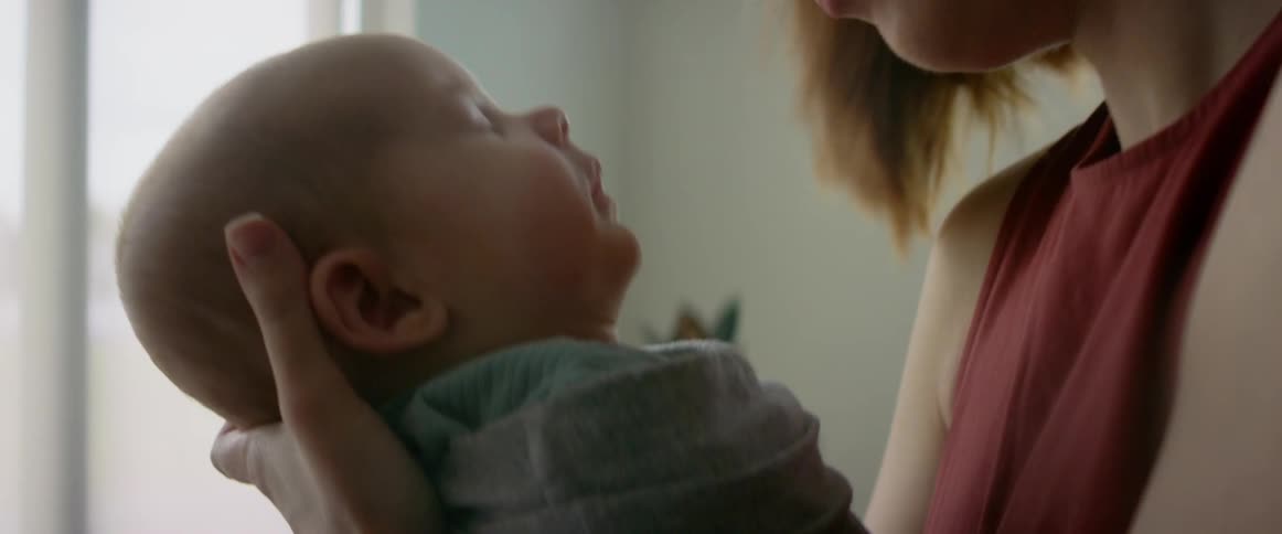 A mother bounces her sleepy swaddled infant son in her hands to try to put him to sleep