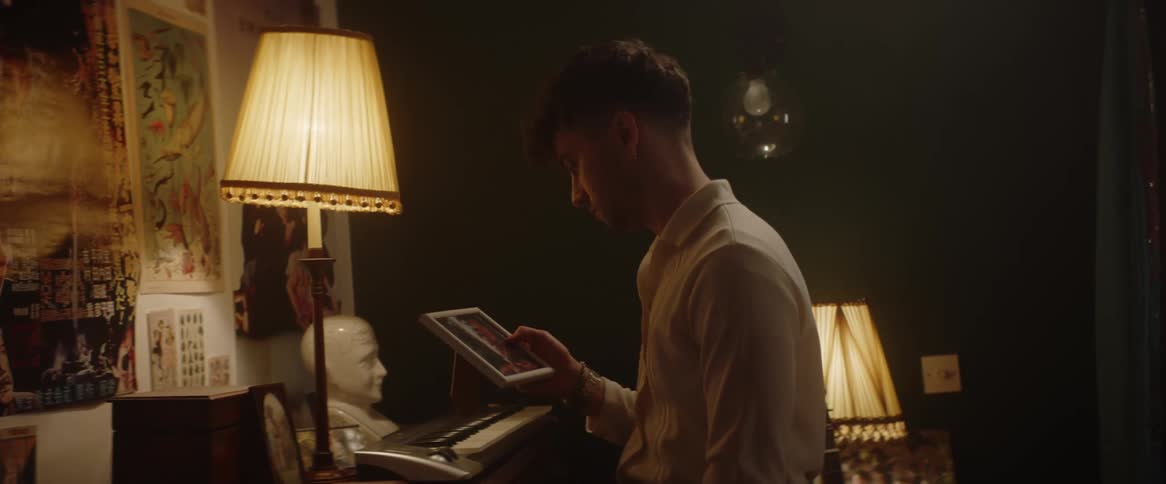 A young man looking sad picks up a photograph and looks at it while standing in the living room