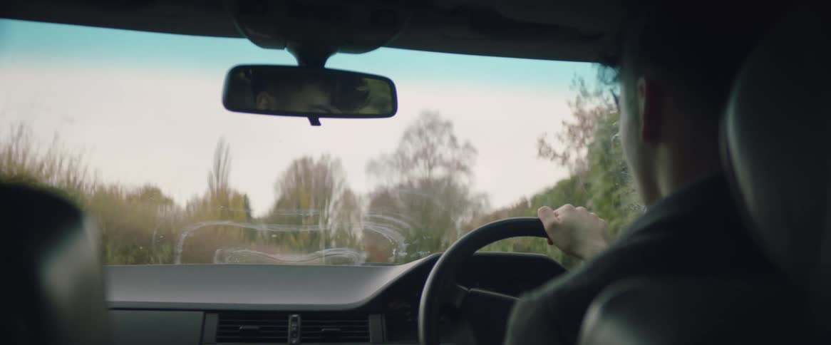 A man is driving an automobile on a country road lined with trees on a fall day