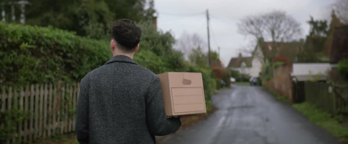 A man is carrying a box as he walks on a neighborhood street