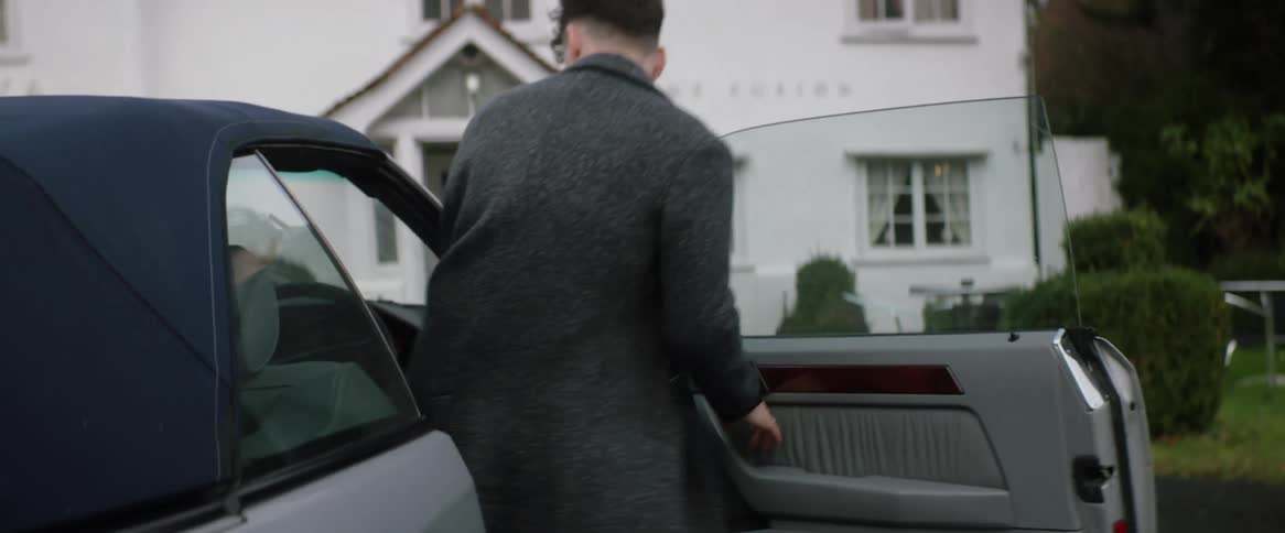 A man opens the door of a car parked in front of his house and he gets inside and closes the door