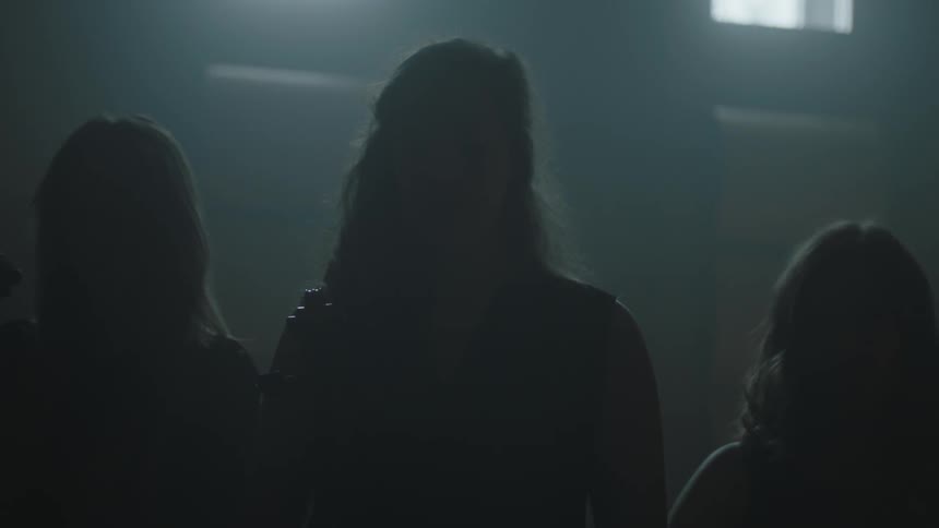 Women holding stringed instruments stand in a dimly lit room
