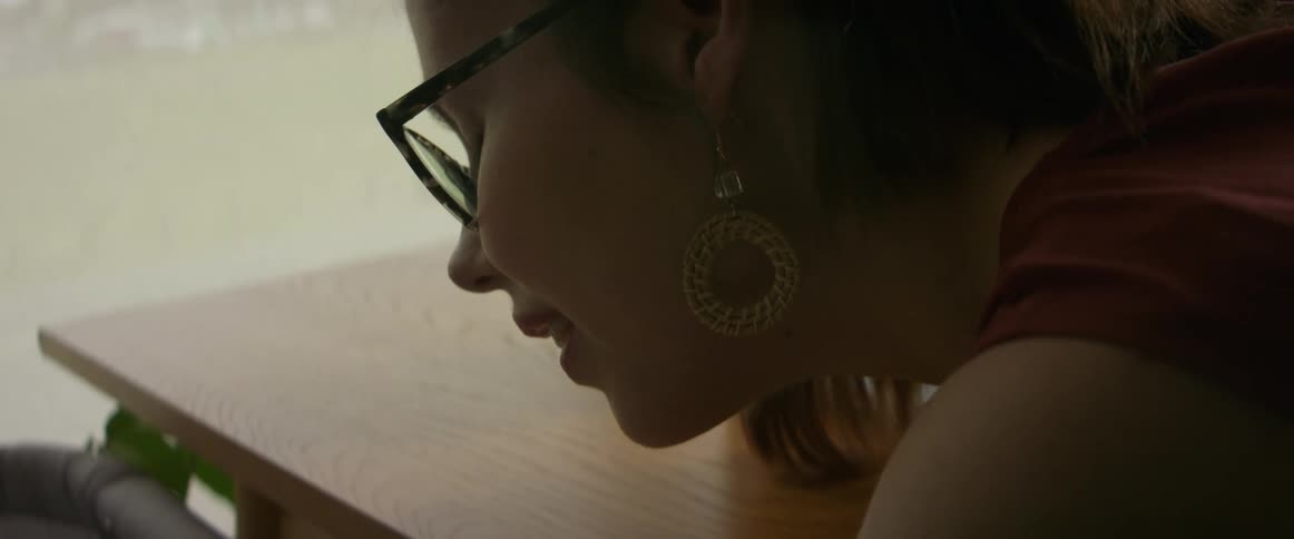 A woman is sitting at a desk with a laptop computer as she talks to her baby in the crib next to the table