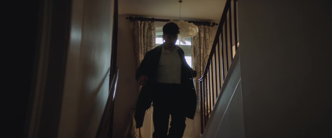 Man with white shirt and black overcoat rush downstairs in house