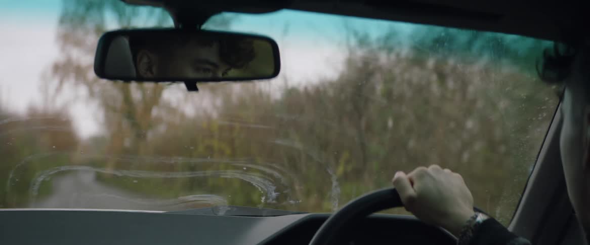 A man is driving an automobile on a country road lined with trees on a fall day
