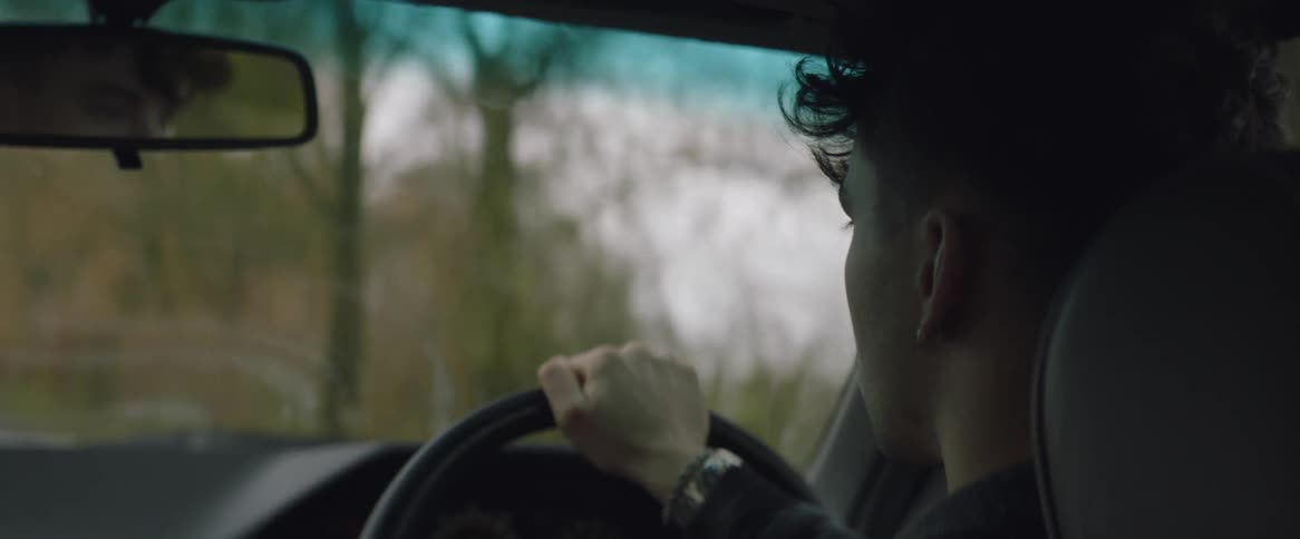An up close of the back of a mans head driving a car as trees go by