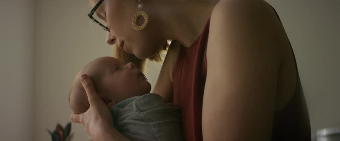 Mother rocking newborn baby to sleep then leaning in to kiss forehead