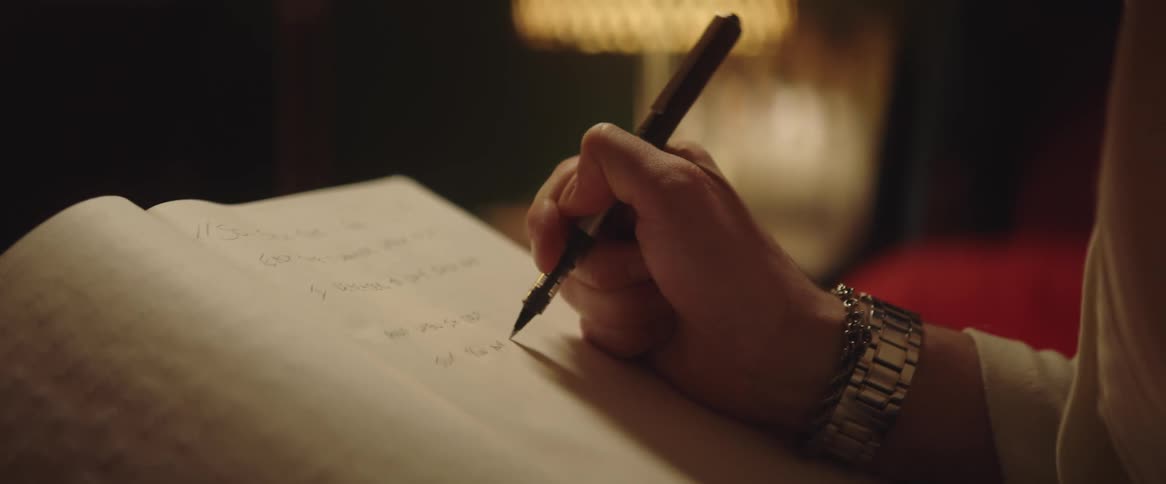 A man is sitting down holding a pen in his hand as he writes in a book