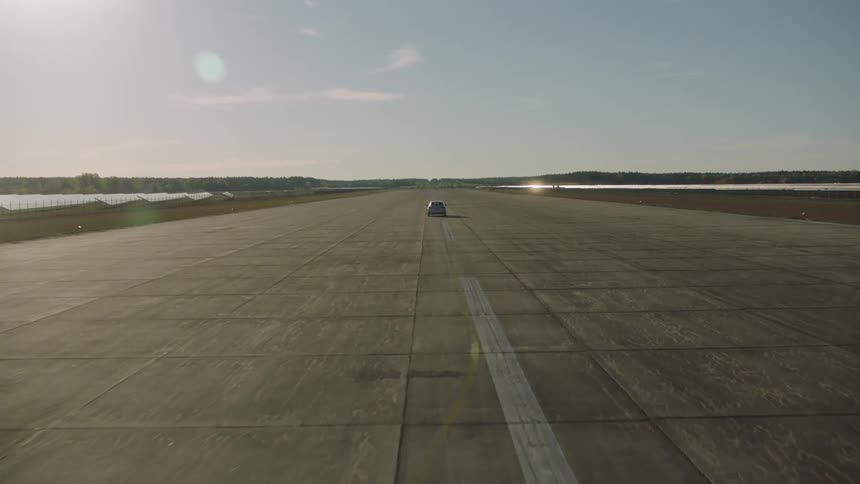 The sun shines brightly as an automobile travels on a wide open empty road