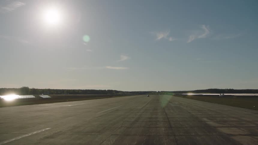 Car drives along runway leading to woods between lakes