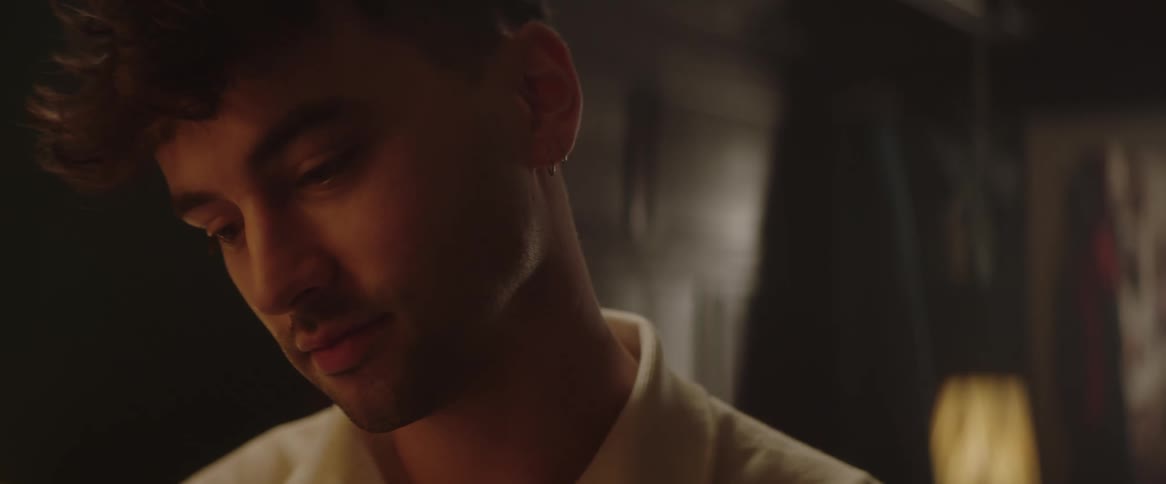 A man is looking down thinking with a look of fondness in his eyes then smiles just slightly as if he has figured out the answer to something that is special to him