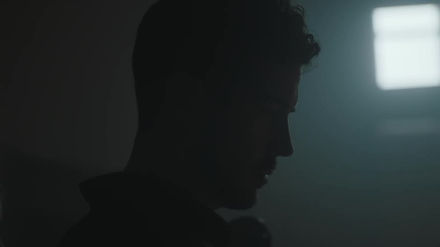 A man stands in a dark area looking down