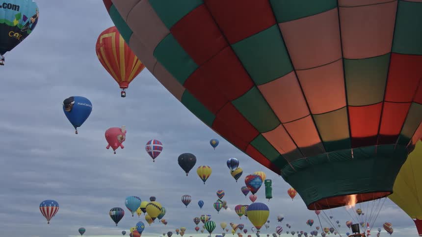 Fire glows inside a hot air balloon as many colorful montgolfier balloons float in the cloudy sky