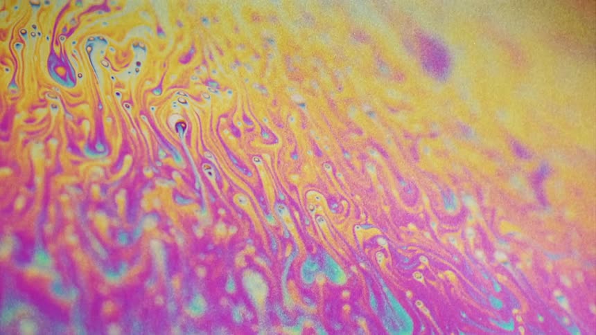 Fluorescent colors move and blend as small particles streak as they float over the surface colors
