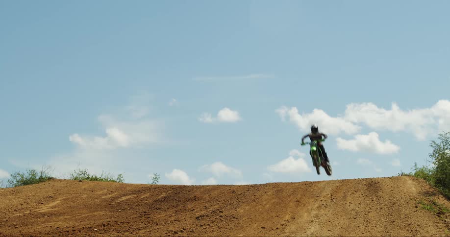 A motocross rider jumps over a dirt hill