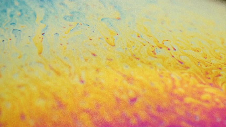 Fluorescent colors move and streaks blend as small particles float over the surface colors as they stretch
