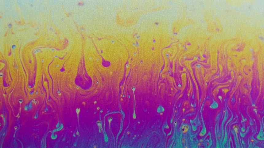 Fluorescent colors move and streaks stretch and blend as small particles float over the surface colors