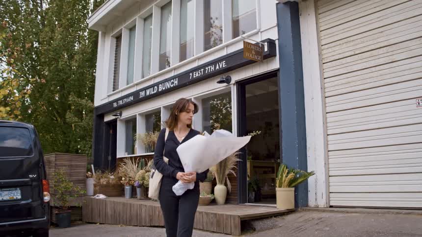 A woman walking out of a flower shop carrying a bouquet