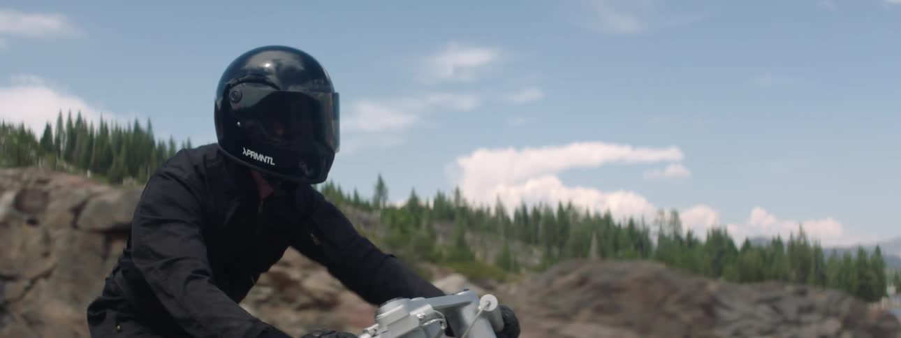 Motorcyclist rides motorcycle along highway past mountains and water