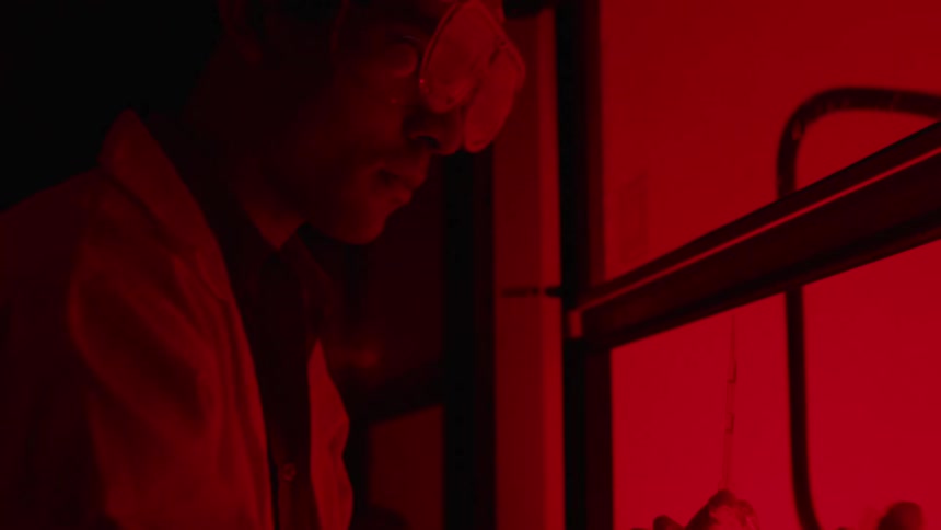 White coated lab worker performs tests in red lit room