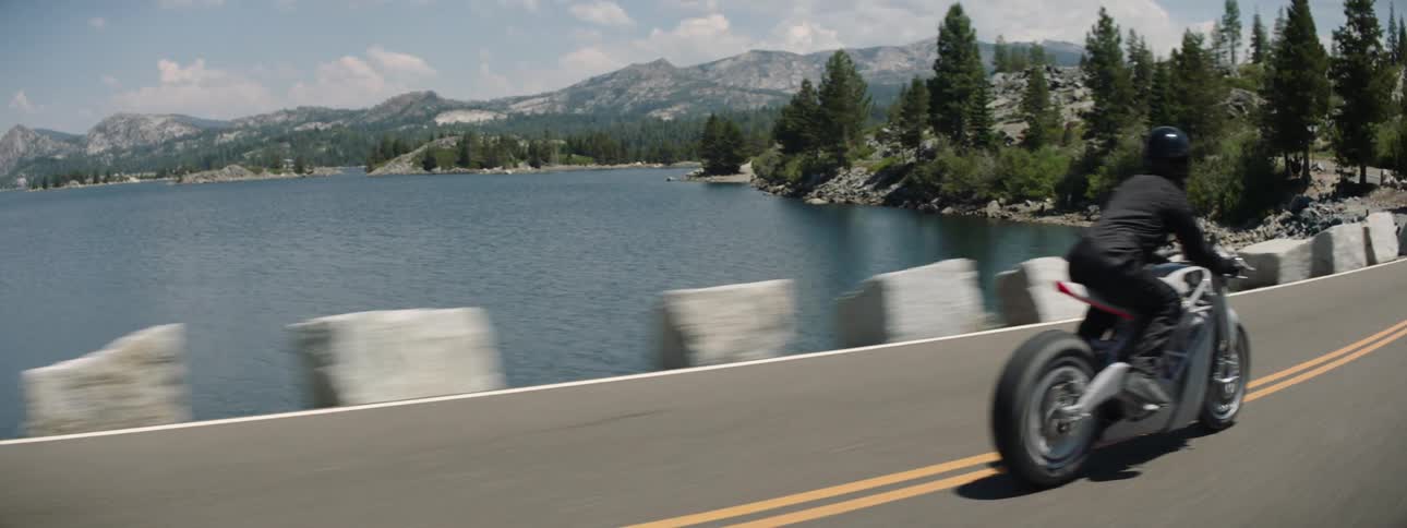 A person wearing a black coat and helmet riding a motorcycle on a road near water
