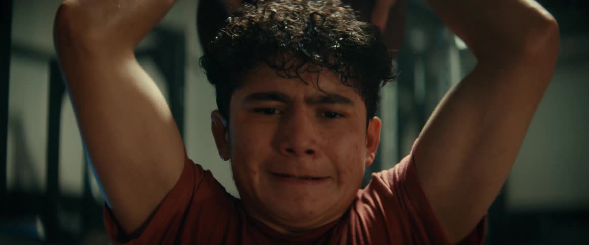 A teenage boy is lifting weights at a gym and really struggling with it