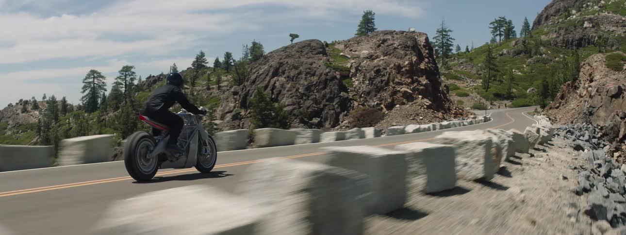 A person riding a motorcycle on pavement with boulders on the side of the road headed into mountians