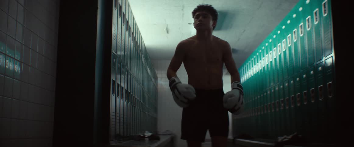A boy with boxing gloves on jumps around and moves his arms in the locker room