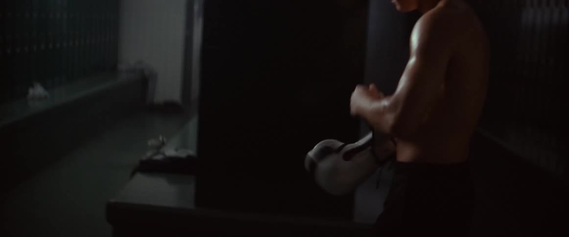 A man angrily throws a boxing glove against a locker in a locker room