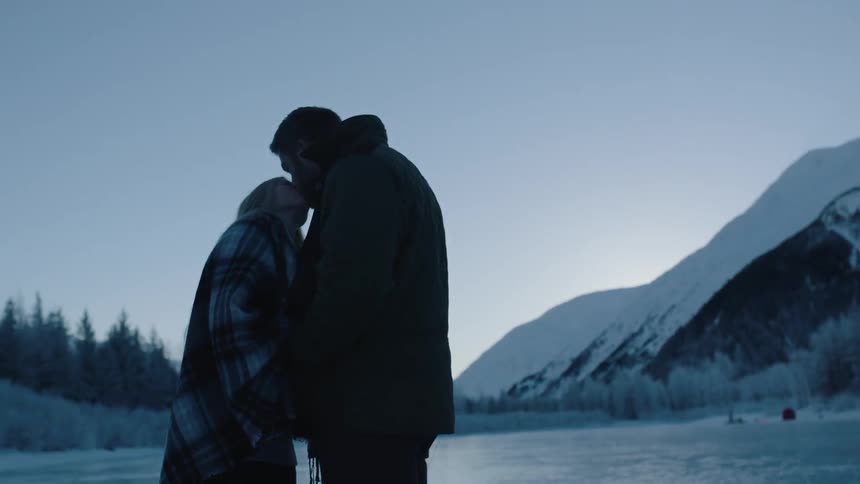 A man and woman kiss by a mountain range