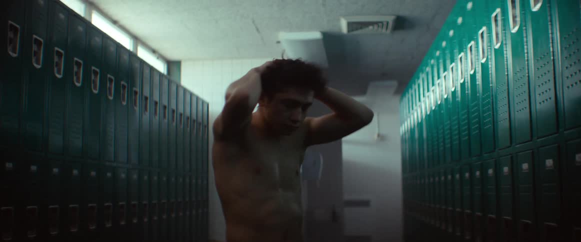 A teenage boy is standing in a locker room as he throws his boxing gloves in a fit of anger and grabs his head with his hands