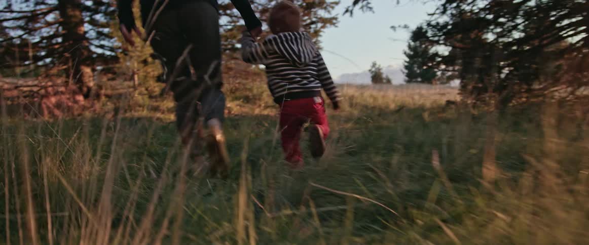 A woman holds her sons hand while running through a field