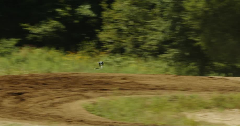 A motocross rider speeds past a dirt trail in a forest