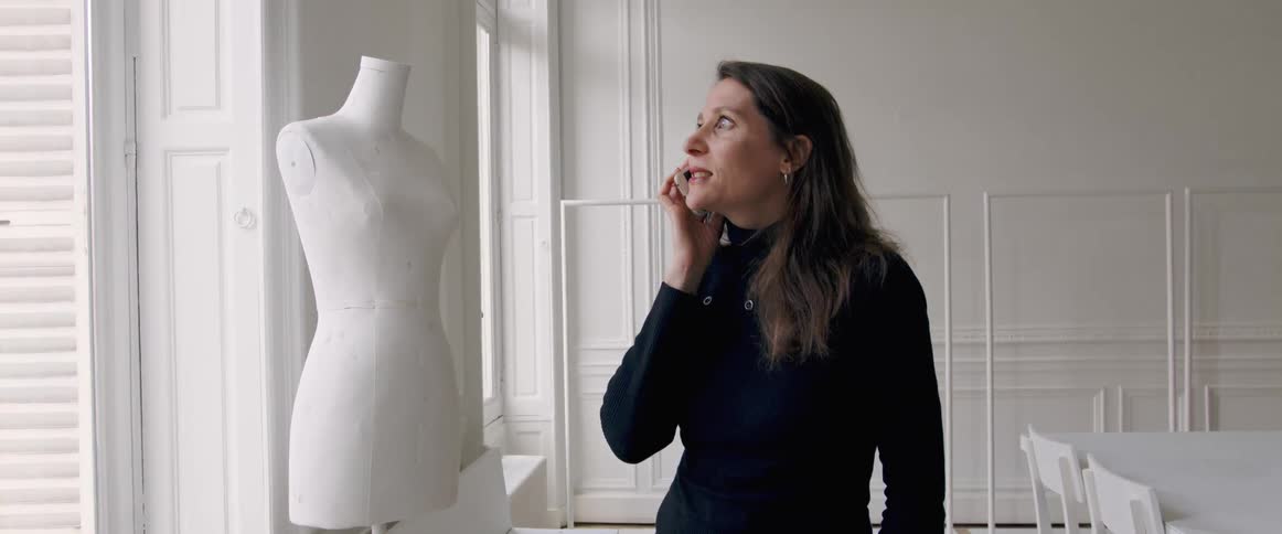 A woman talks on the phone while standing next to a dress form