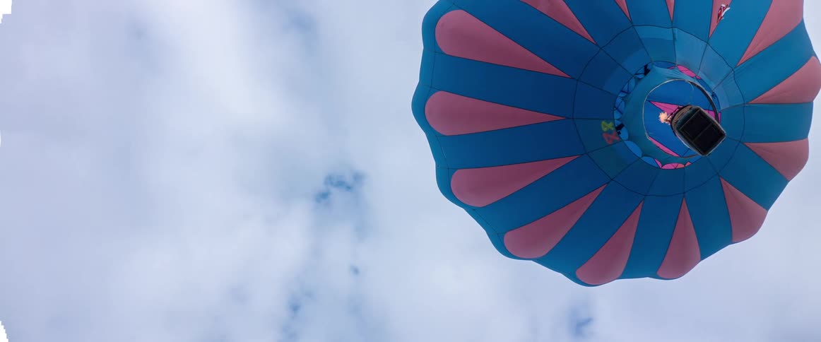 Hot air balloon rises in cloudy sky as flame is applied